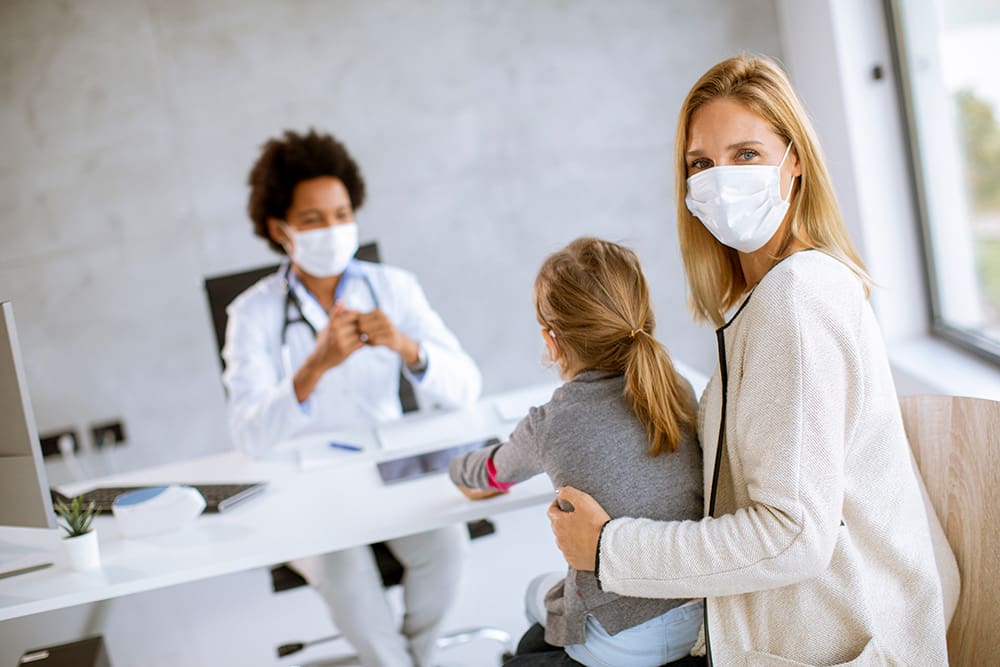 A woman holding a child in a medical mask discussing healthcare SEO with the doctor.